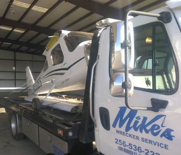 Airplane on a flatbed tow truck from Mike's Wrecker Service in Alabama. The plane is white with black and yellow accents.
