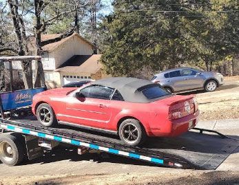 Red convertible Mustang on a tow truck. A silver SUV is parked nearby.