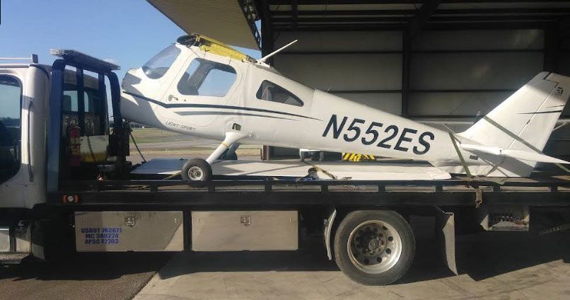 A small, white airplane with black stripes, serial number N552ES, is being transported on a tow truck.