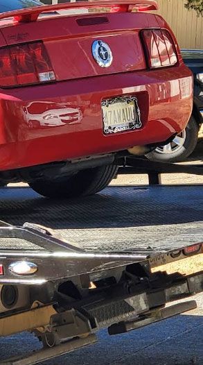 Red Ford Mustang on a tow truck, license plate visible.