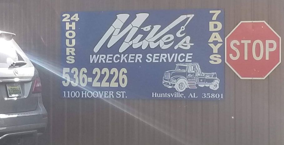 Sign for Mike's Wrecker Service in Huntsville, AL, with phone number and truck graphic. A stop sign is nearby.