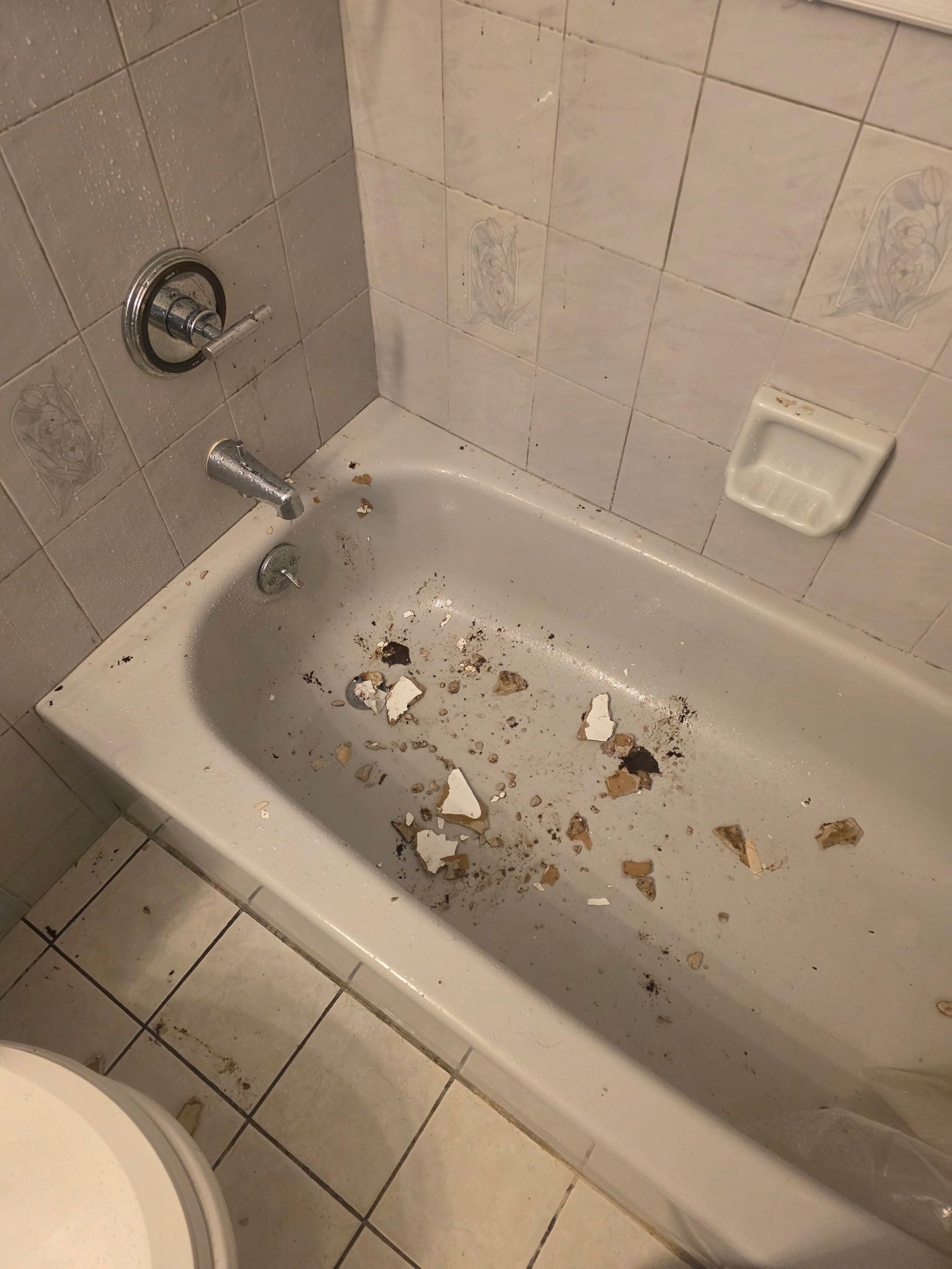 Dirty bathtub with debris and broken pieces scattered inside a tiled bathroom.