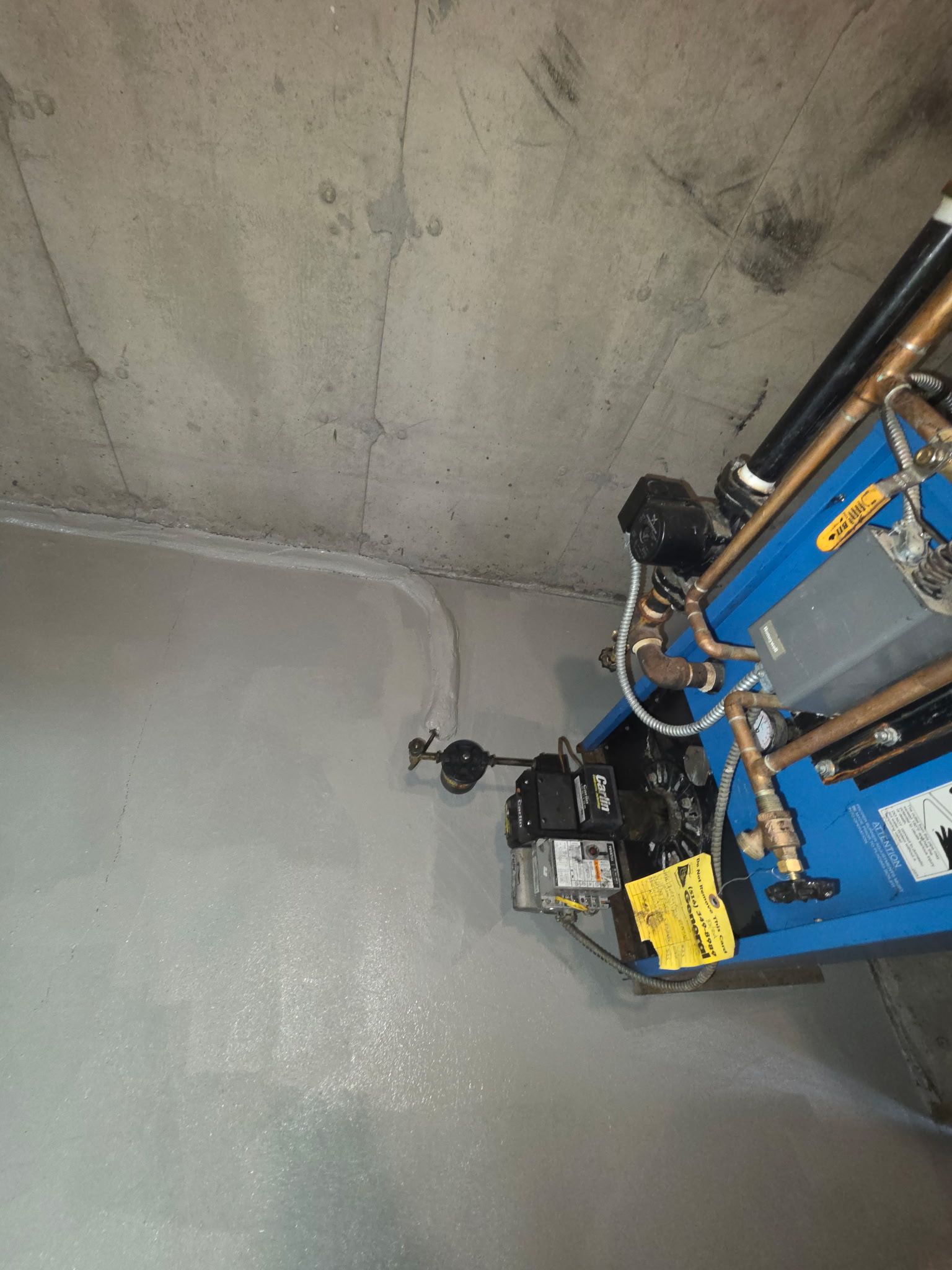 Concrete wall and ceiling corner with a blue utility lift and attached equipment indoors.