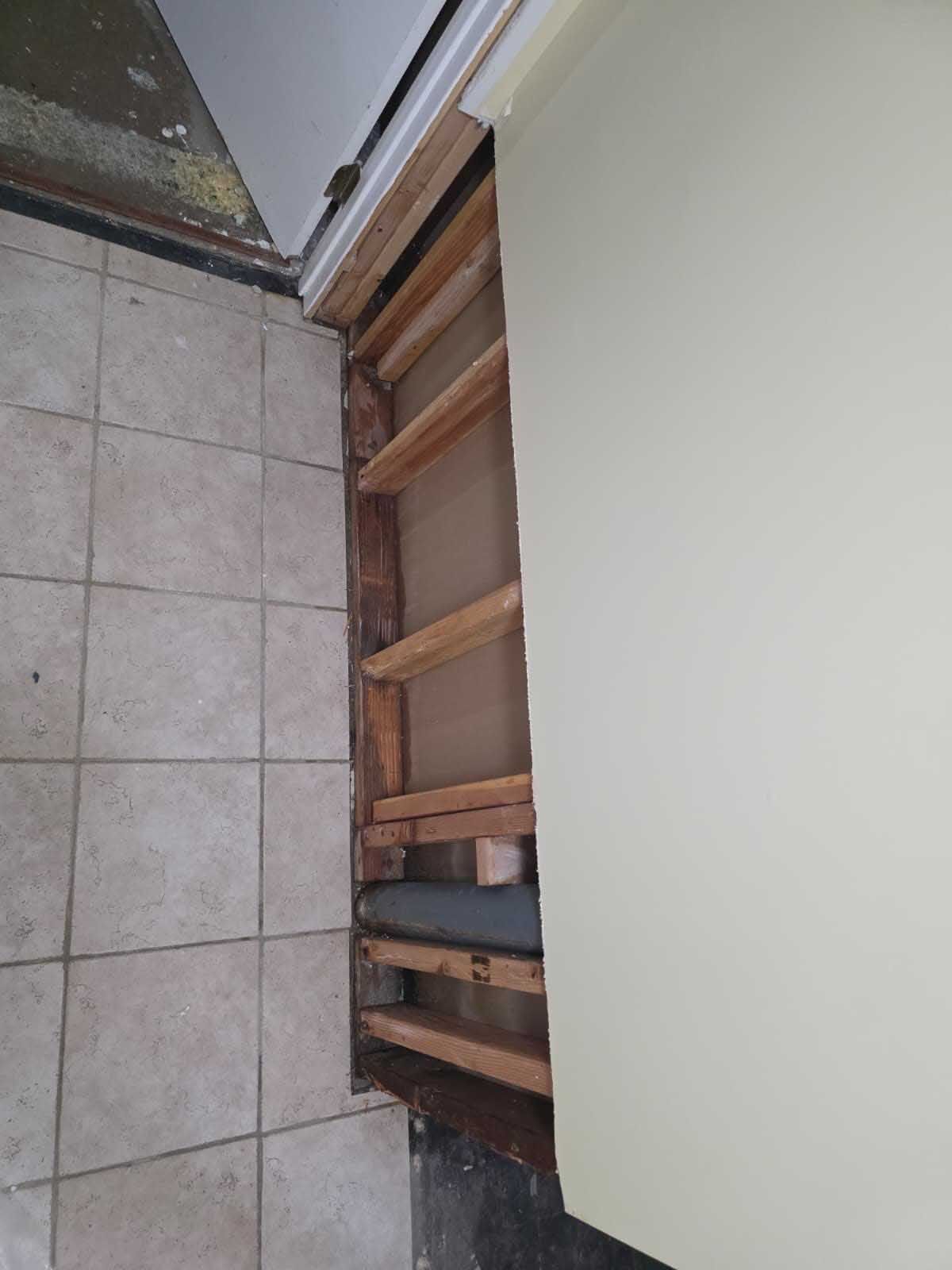 An exposed, unfinished wall frame with wooden studs next to a tiled floor and a door frame.