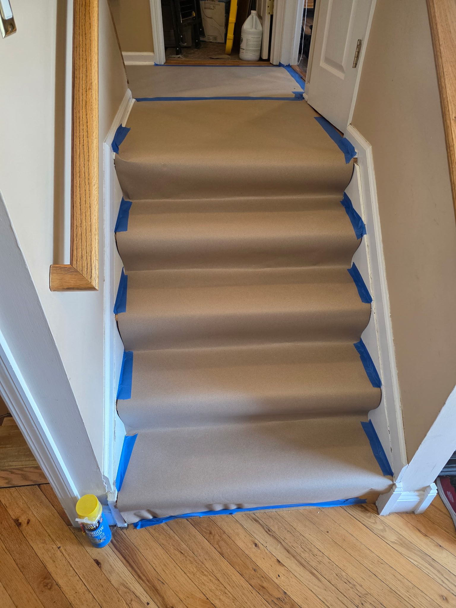 Staircase covered with brown protective paper, blue painter’s tape, and plastic sheeting in a hallway