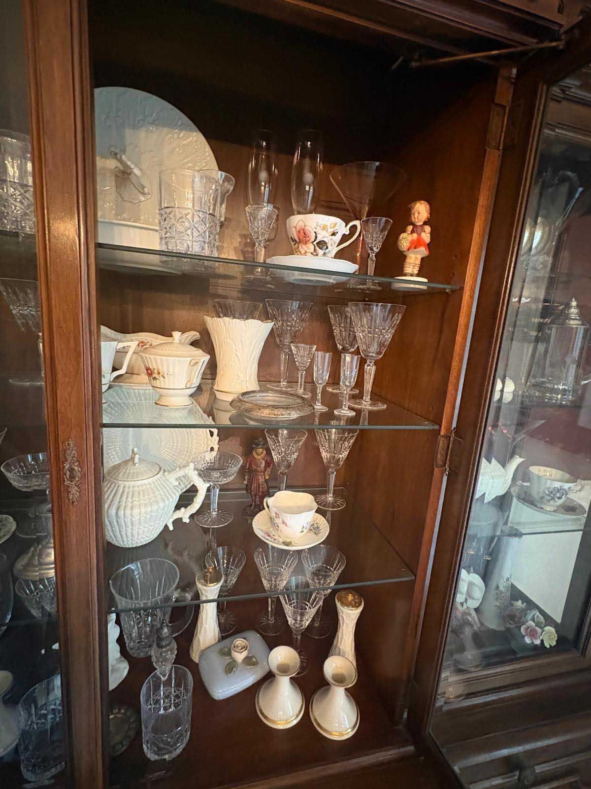 A wooden china cabinet display case filled with various crystal glassware, white porcelain dishes, and decorative items.