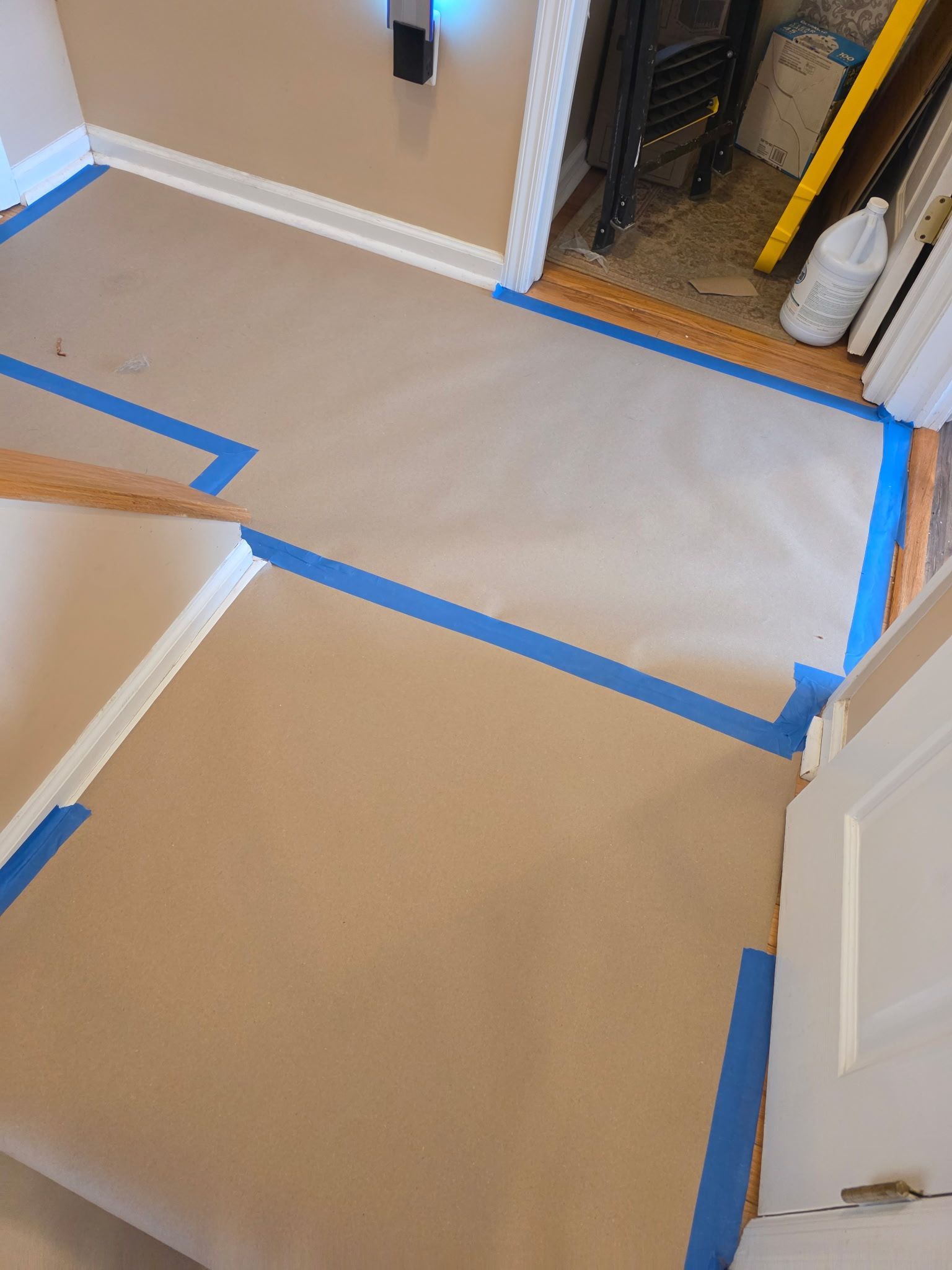 Hallway and doorway floor covered with brown paper and blue painter’s tape for protection during painting