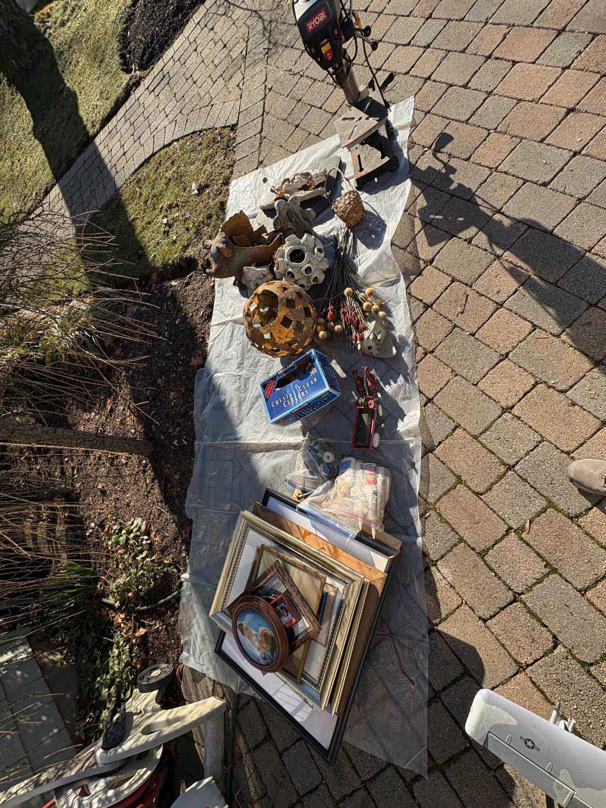 A collection of scattered items, including frames, electronics, and small objects, lying on a plastic sheet on brick pavers.