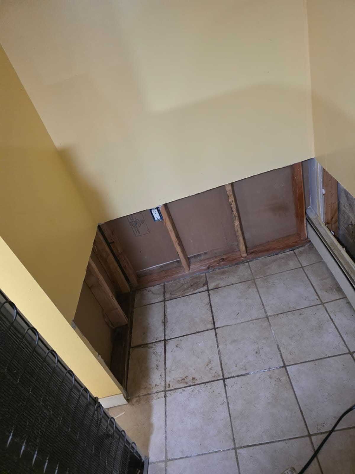 An interior corner with yellow walls and tile flooring, showing an open section of wall framing exposing the studs.