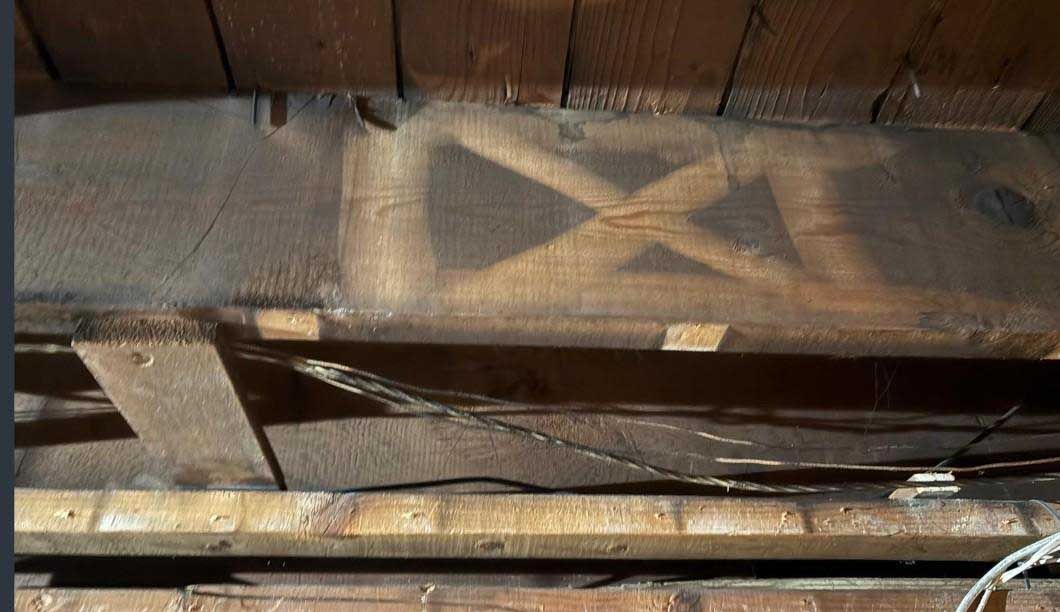 A dark wooden beam in an attic features a large, faded 