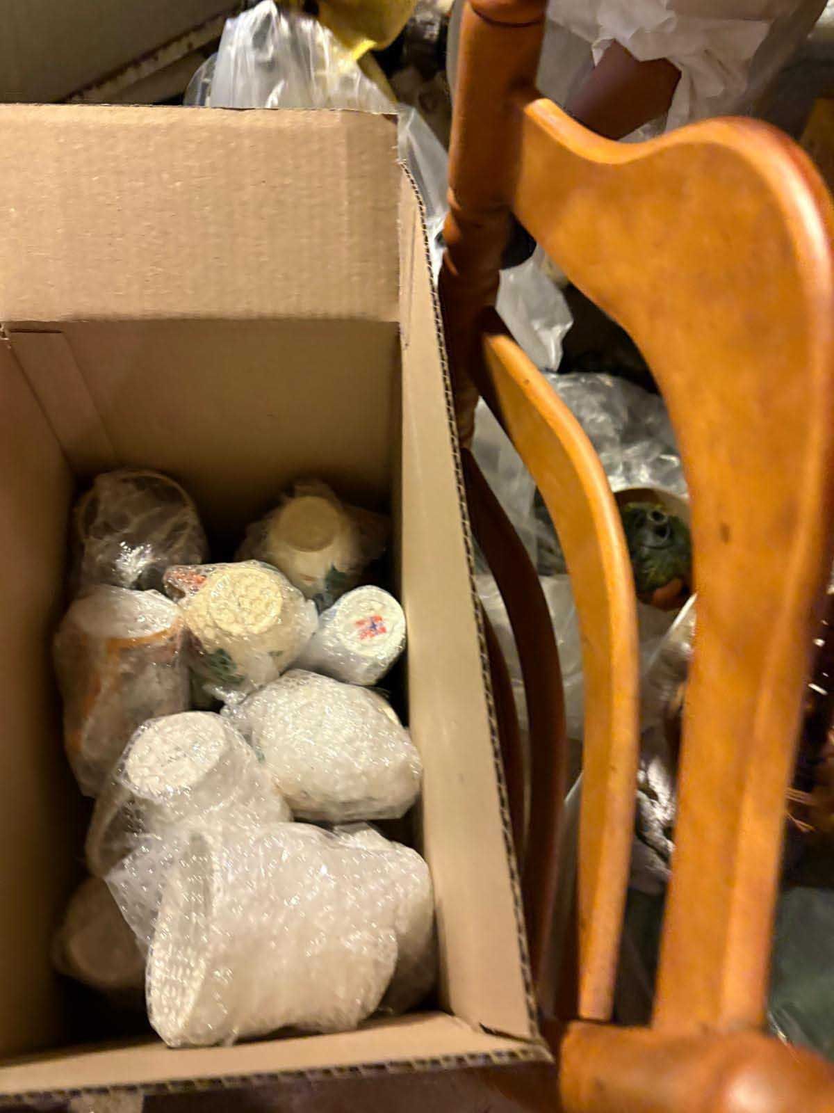 A cardboard box filled with several bubble-wrapped items, sitting next to a wooden chair.