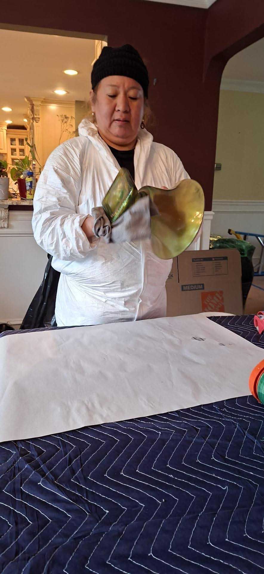 A person wearing a white protective suit and black beanie holds a brass horn over a table covered in white paper.