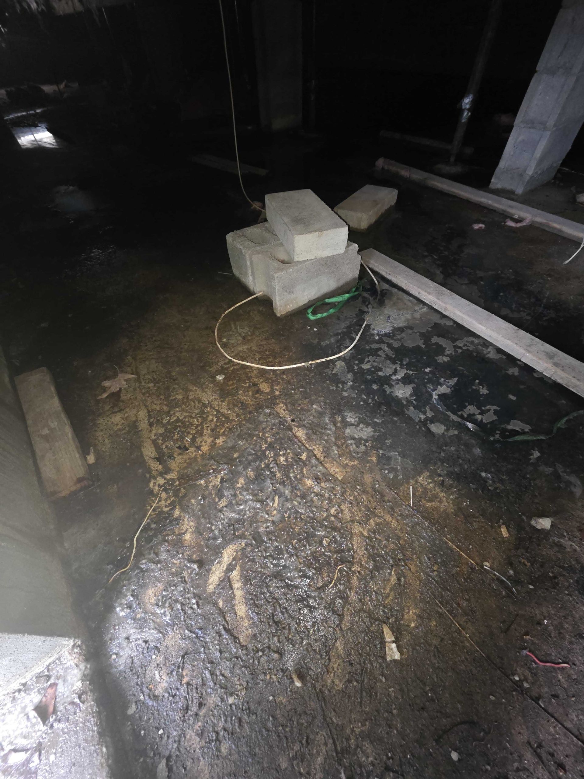 Dark, cluttered construction site floor with scattered cinder blocks, debris, and a coiled wire in the center.