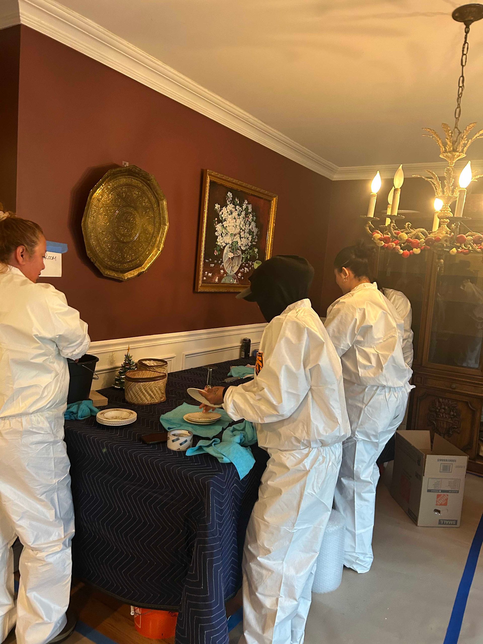 Three people in white hazmat suits work at a table with a dark tablecloth in a room with deep red walls.