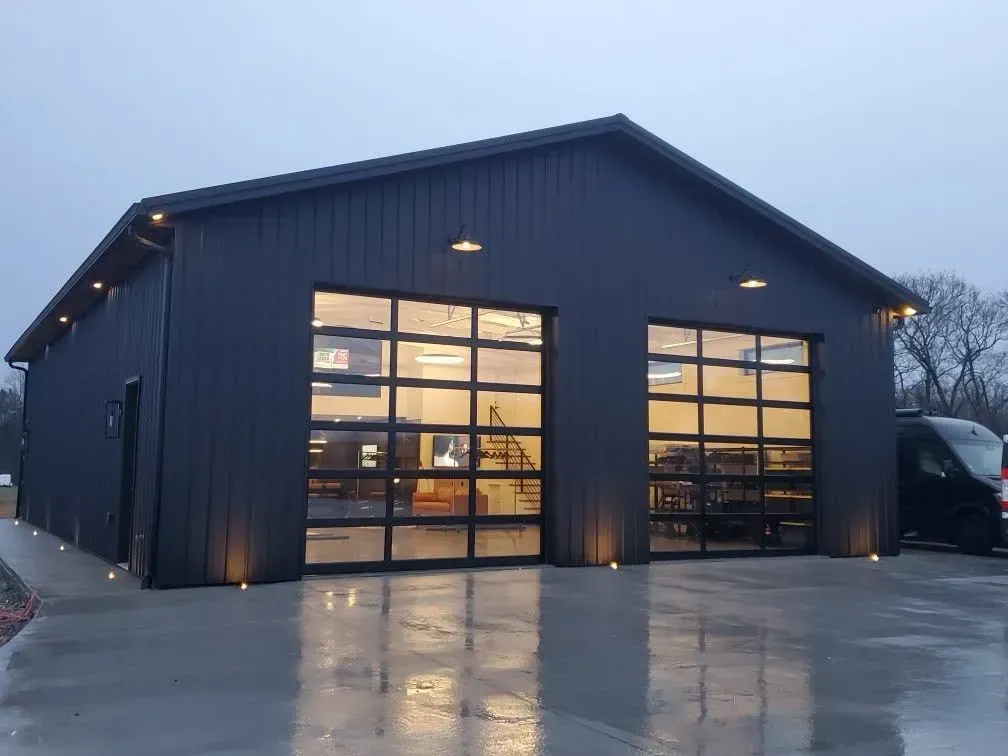 Dark gray building with glass garage doors, illuminated by exterior lights on a wet surface.
