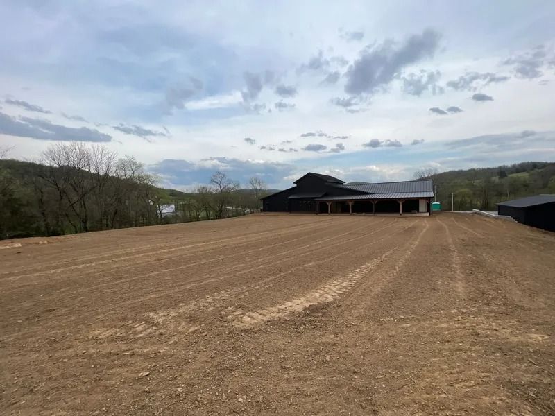Cleared field with a large black barn under a cloudy sky.