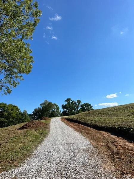 Gravel road ascending a grassy hill under a bright blue sky.