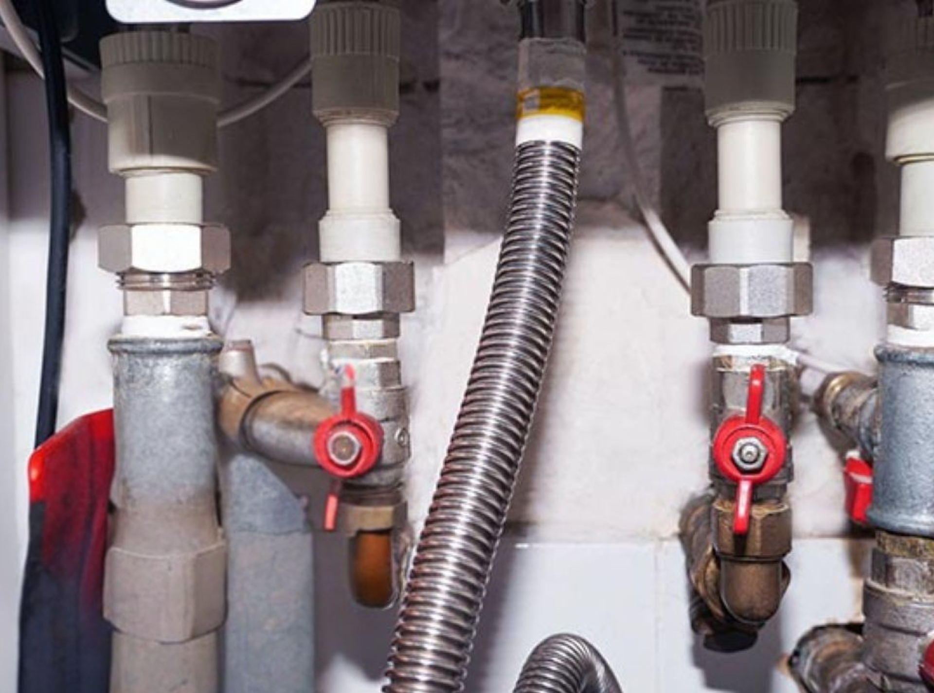 A top-down view of copper plumbing pipes and fittings with three red-handled valves against a white background.