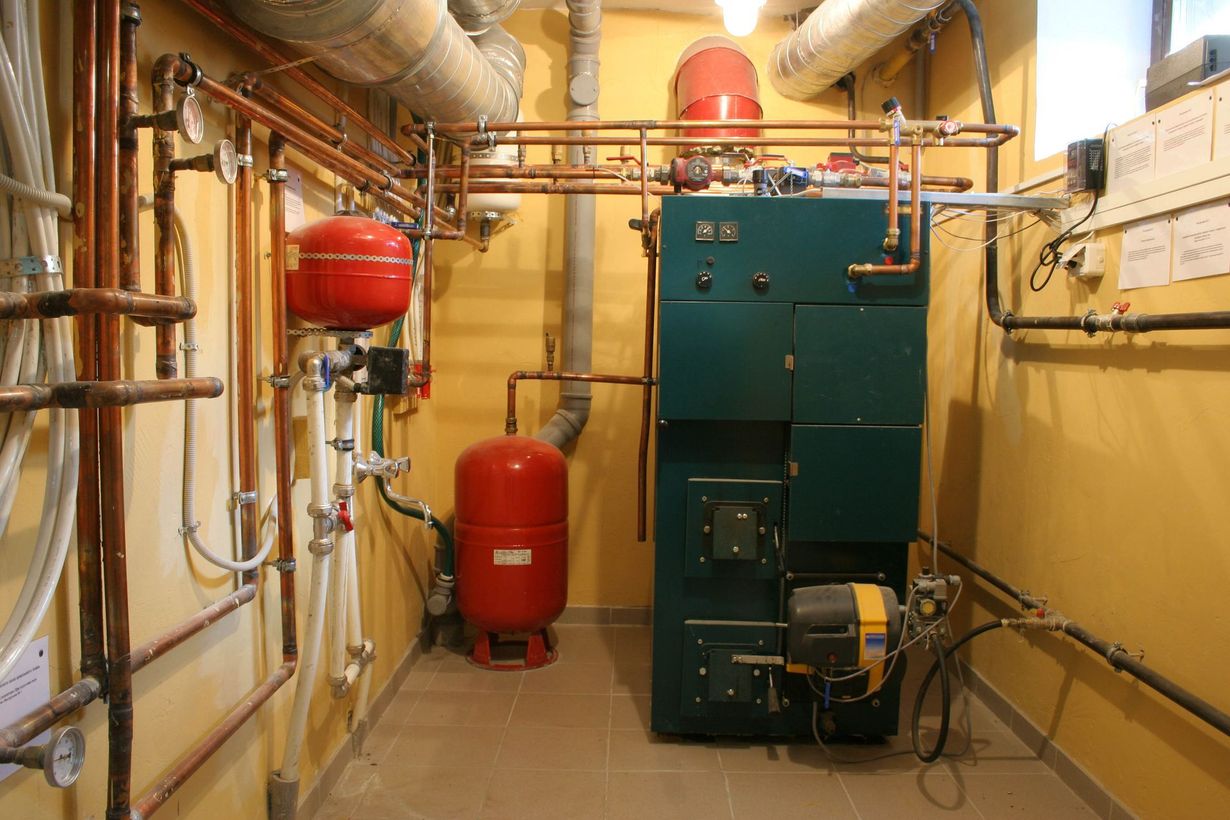 A Rinnai tankless water heater mounted on a concrete wall with connected copper pipes and a blue expansion tank.