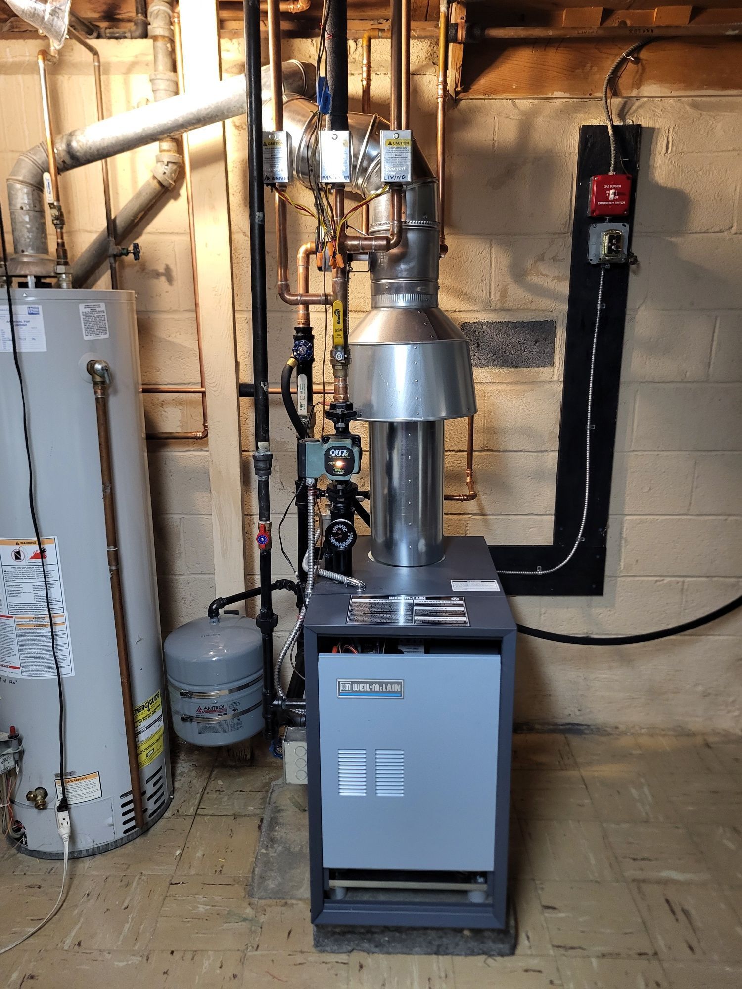 Basement utility room with furnace, water heater, and vent pipes against cinderblock wall