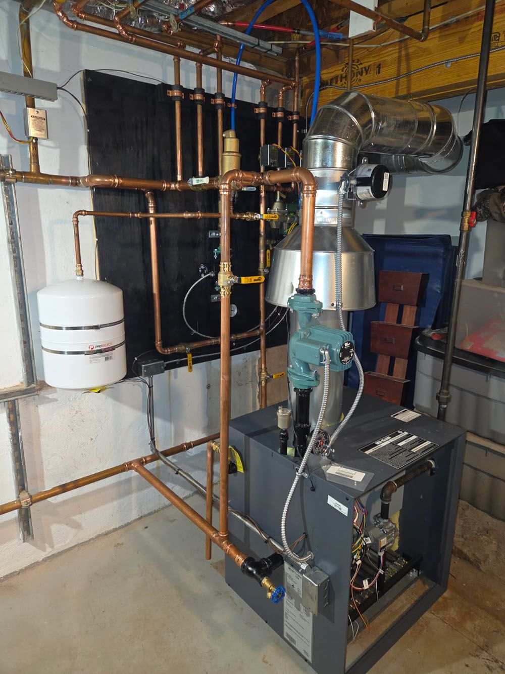 Boiler room with copper pipes, black tank, and furnace equipment in a basement utility area.