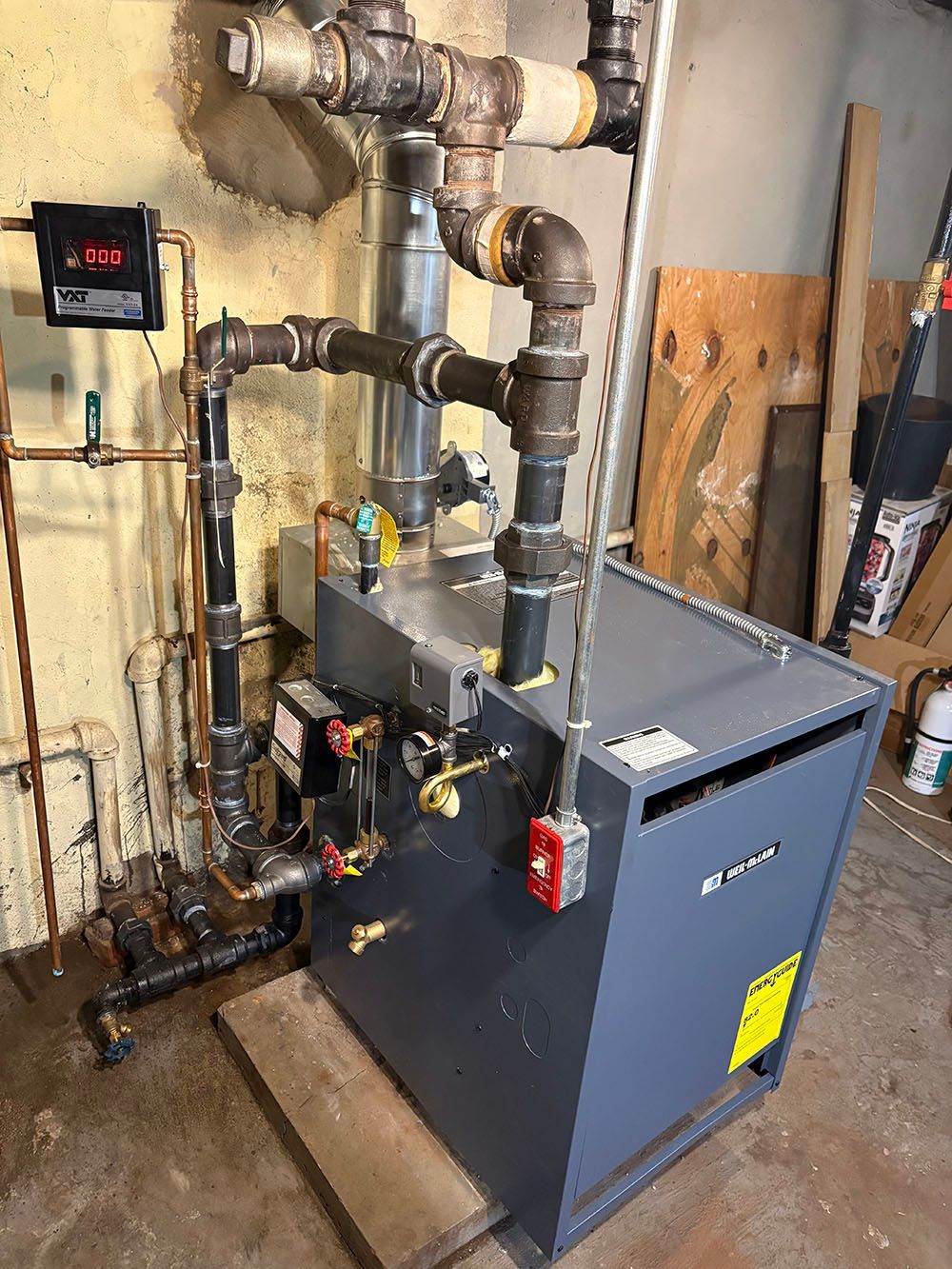 Industrial boiler and piping system in a basement utility room with a blue unit and exposed pipes.