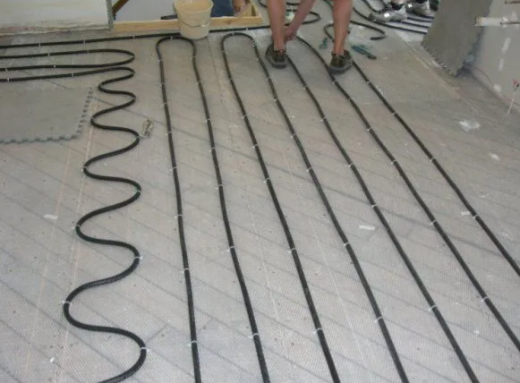 Black tubing laid on a floor, likely for radiant heating. A person stands nearby.