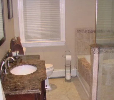 Bathroom with a sink, toilet, tub, and window with blinds. Beige walls and tiles.