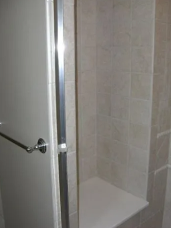 Shower stall with a white door and beige tiled walls, a built-in bench.