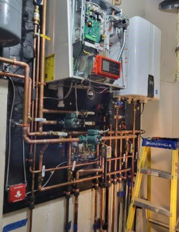 Copper pipes and heating equipment installed on a wall with a ladder on the right.