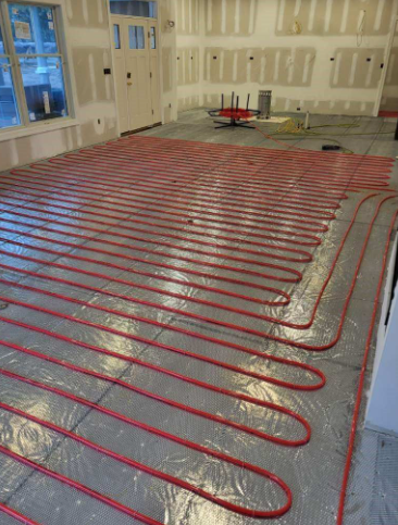 Red radiant floor heating pipes installed across a room, ready for concrete.