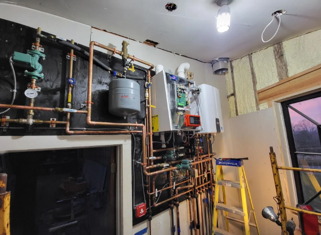 Copper pipes and heating equipment installed on a wall, with a ladder and lighting visible.