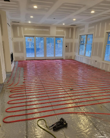 Red tubing for radiant floor heating installed in a room with unfinished walls and drywall.