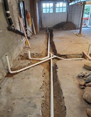 Interior basement under construction, plumbing pipes laid in trenches, near a door.