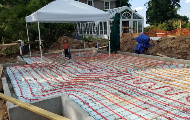 Concrete foundation with red radiant heating tubes. A white tent, house, and greenhouse are in the background.