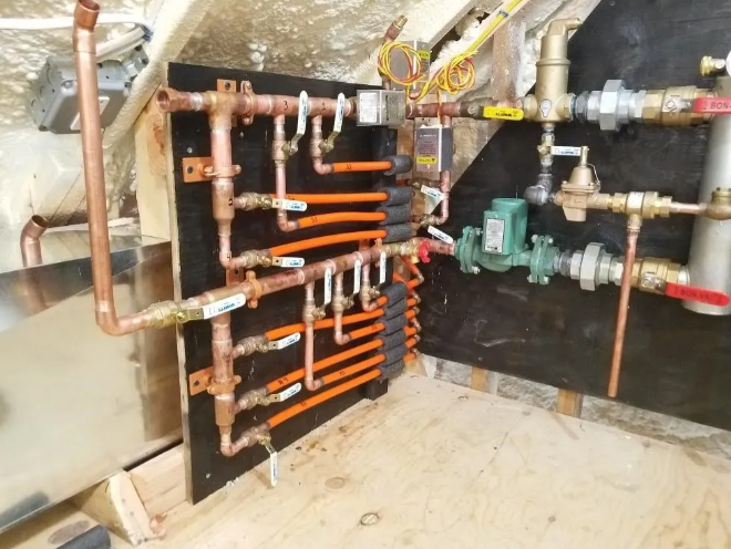 Copper pipes and valves, orange tubing on a wooden board, part of a heating system.