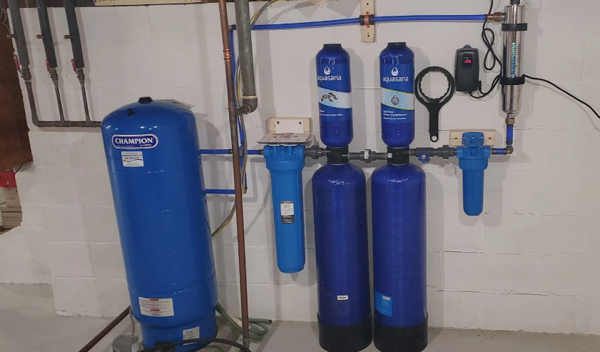 Blue water filtration system components mounted on a white wall in a basement.