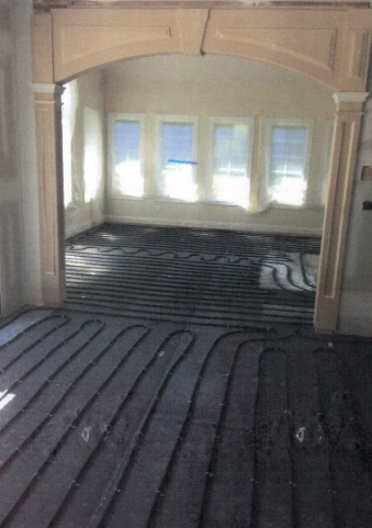 Radiant floor heating system installation in a room with an arched doorway and windows.