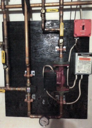 Copper pipes, pump, and valves mounted on a black panel. Pressure gauge at the bottom.