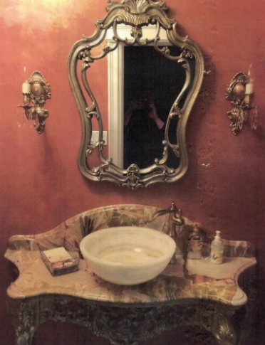 Ornate bathroom vanity with marble sink, decorative mirror, sconces, and red walls.