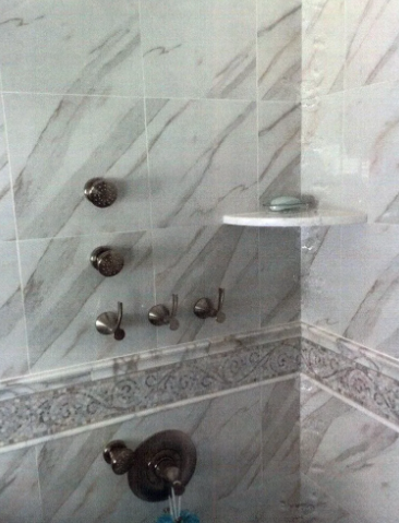 Shower with marbled tiles, various bronze showerheads and hooks, and a soap dish.