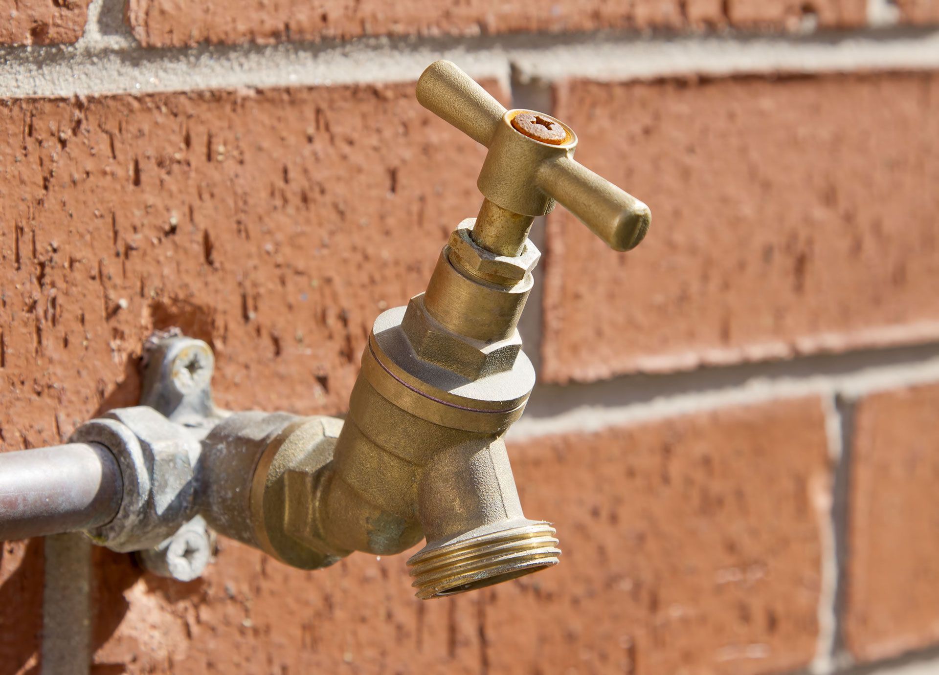 A brass-colored outdoor water spigot mounted on a red brick wall.