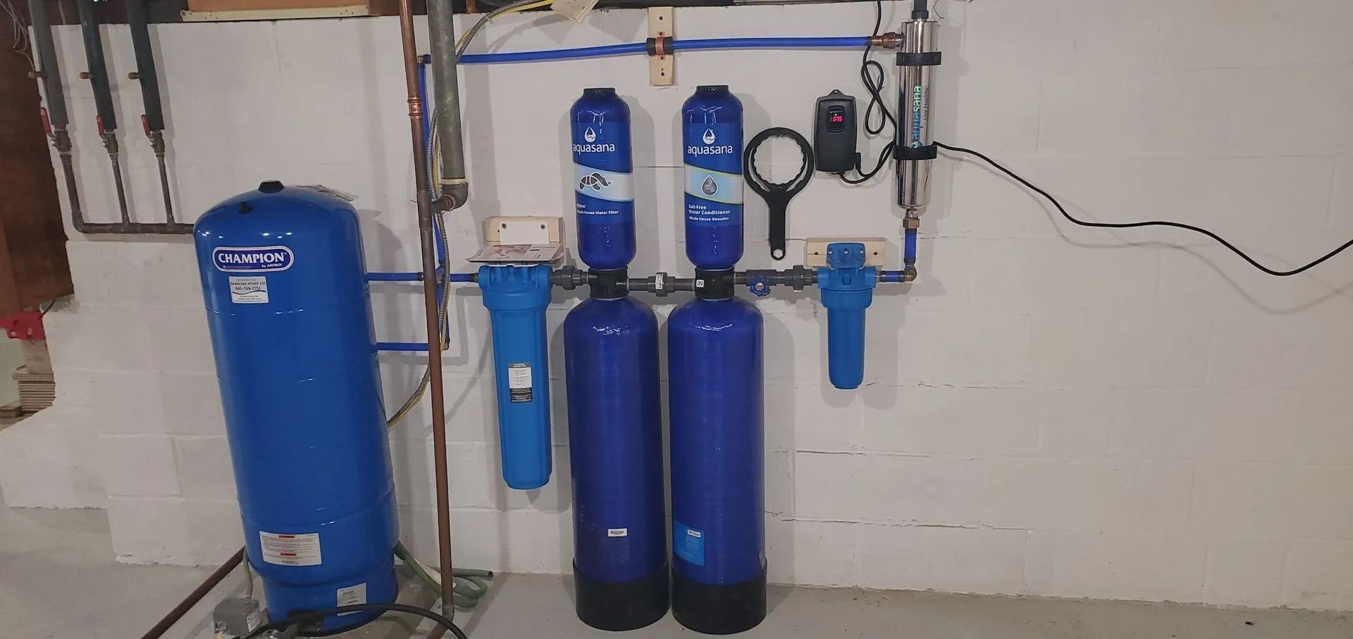 A water filtration system with blue tanks and filters mounted on a white wall in a basement.