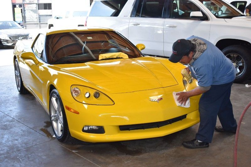 A man is cleaning the front of a yellow sports car
