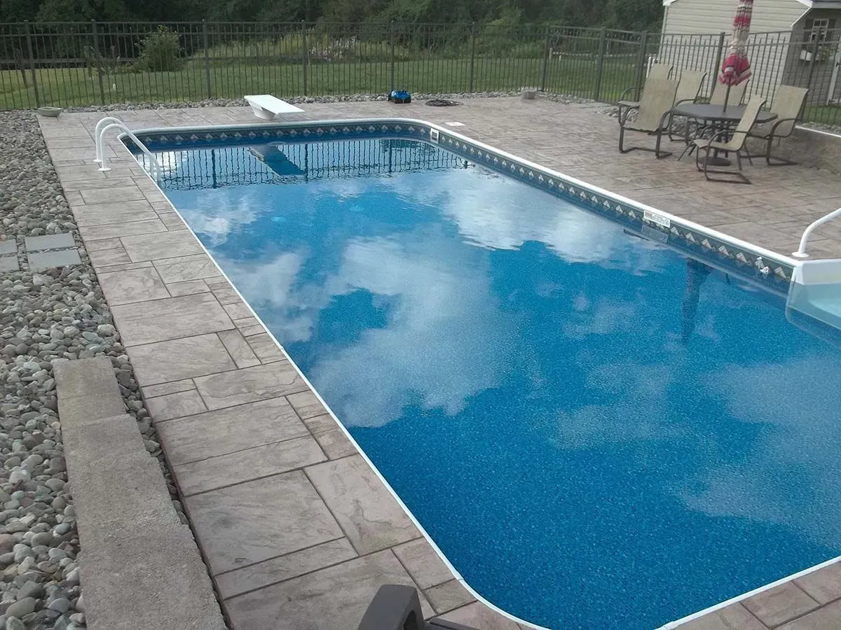 Rectangular in-ground pool reflecting a cloudy sky, surrounded by stone and gravel patio.