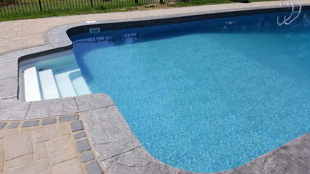 Pool with white steps and blue water, surrounded by gray stone.