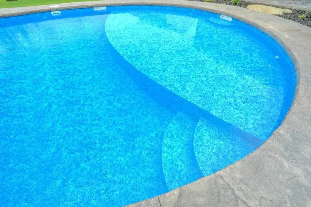 Blue swimming pool with built-in stairs, edged by a stone patio.