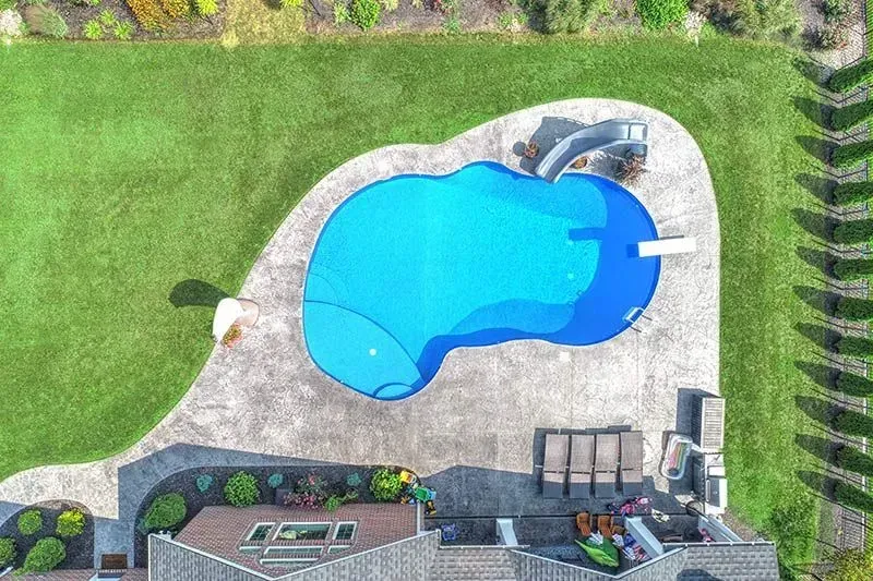 Aerial view of a swimming pool with a slide, surrounded by concrete patio and green lawn.