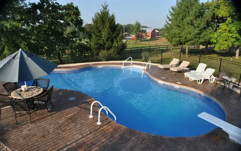 Pool with patio furniture, blue water, and a diving board. A red barn is visible in the background.