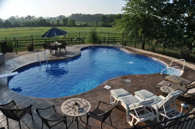 A kidney-shaped swimming pool with a diving board, surrounded by a patio with lounge chairs and a table.